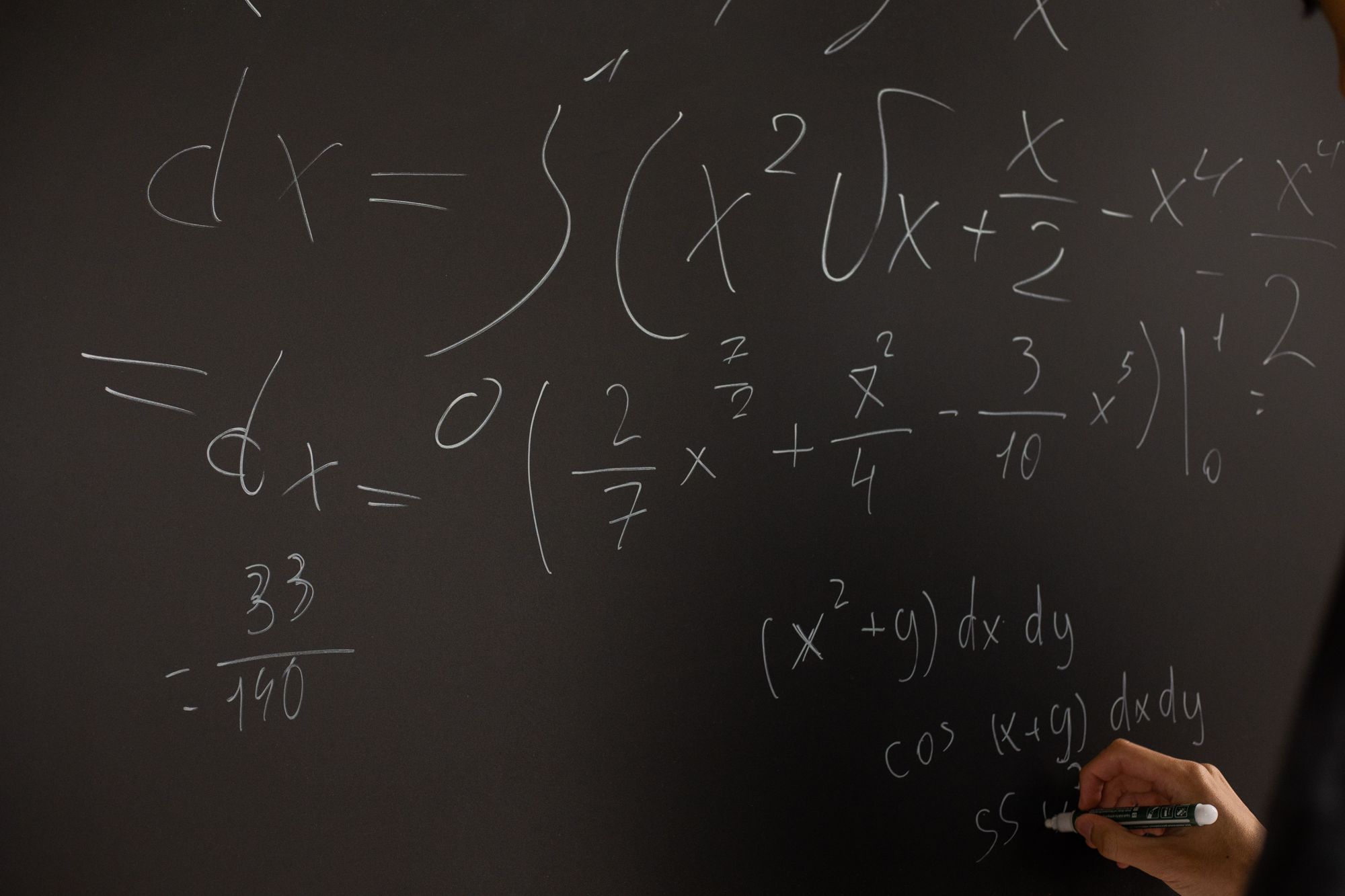 Calculus integrals worked in chalk on a blackboard, a hand writing in the corner