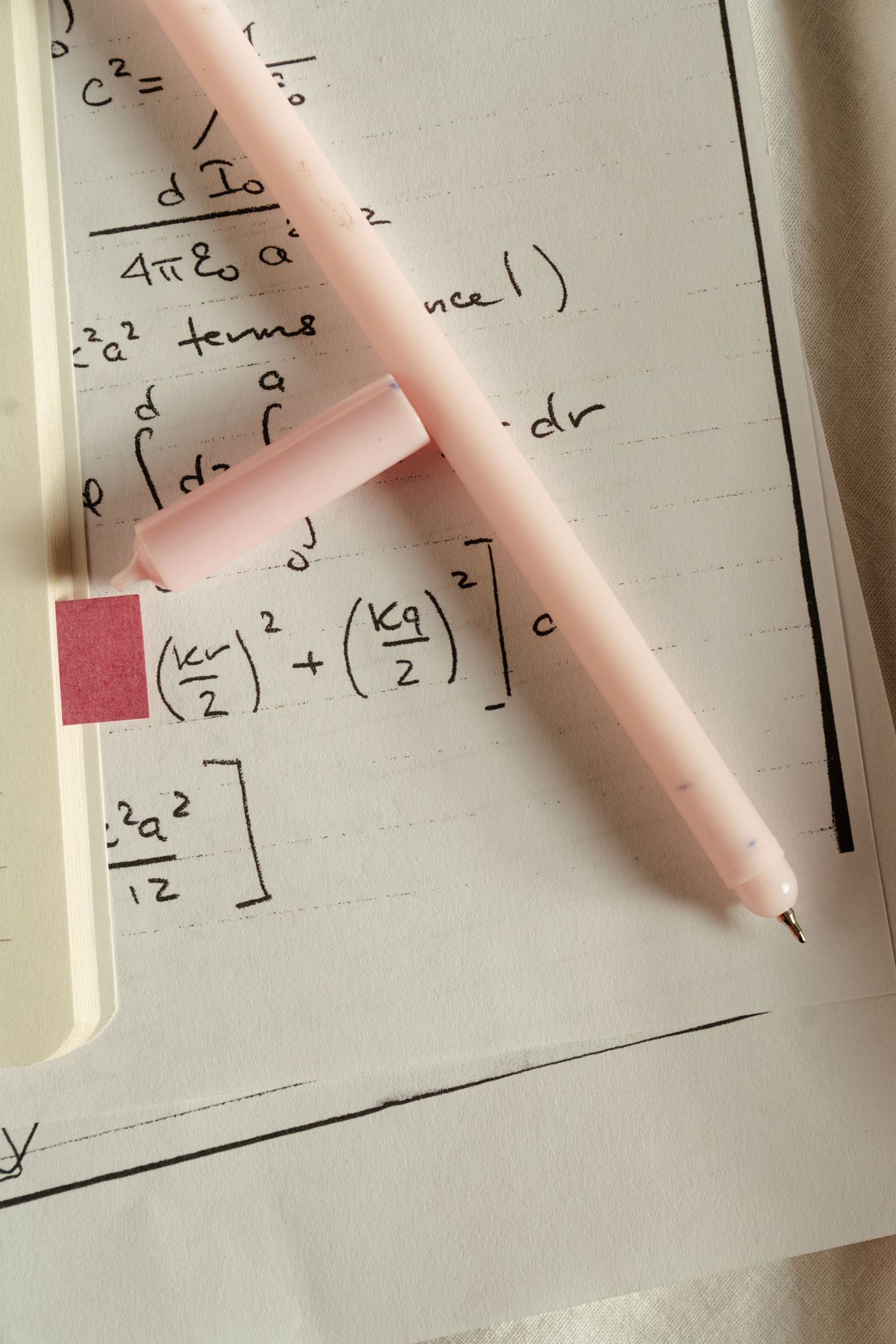 Handwritten electromagnetism equations on lined paper with a pink pen lying across them