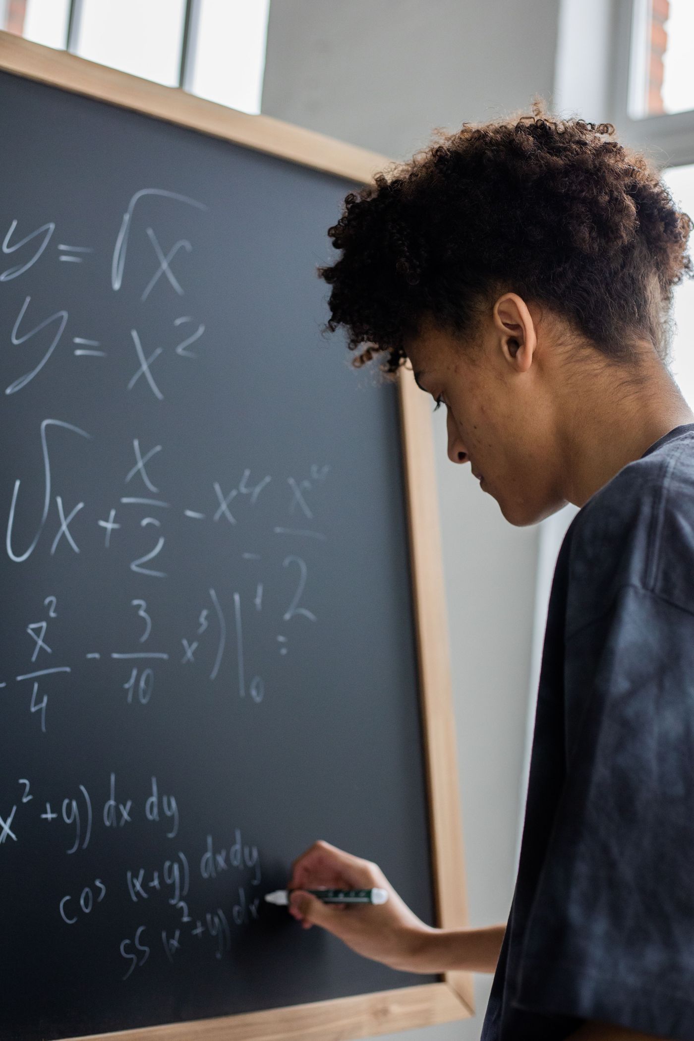 A student writing calculus equations in chalk on a blackboard