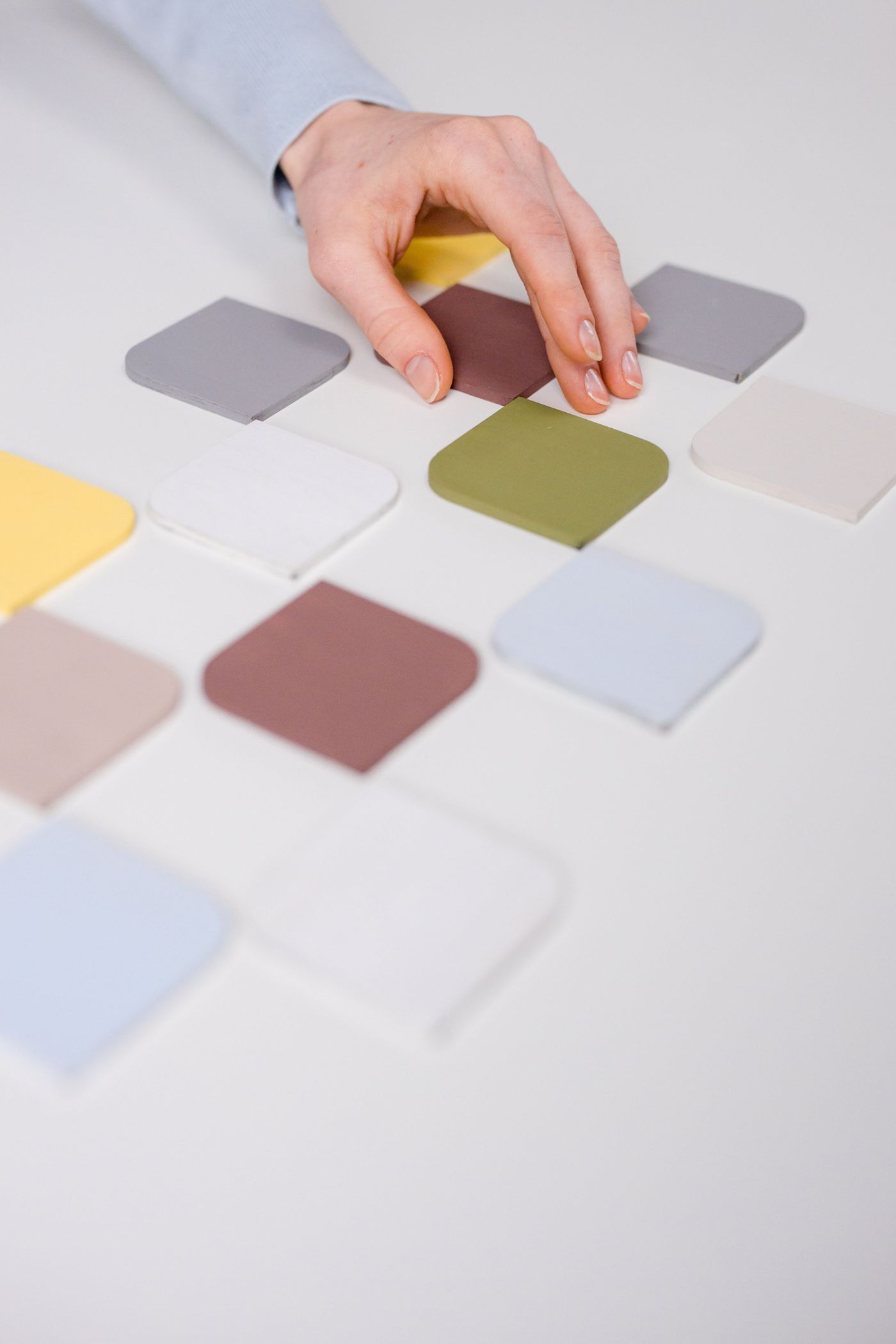 A hand picking one colour swatch out of a grid of swatches on a white table