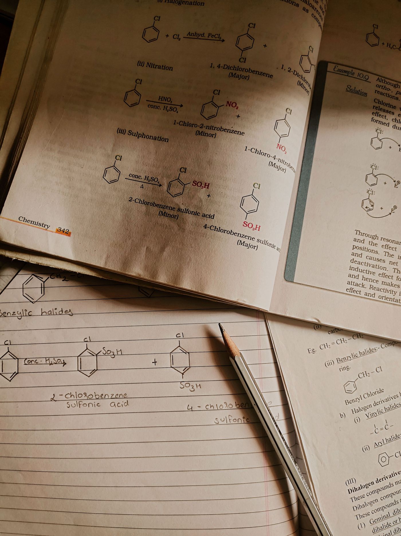 An open chemistry textbook showing chlorobenzene reactions beside handwritten notes and a pencil