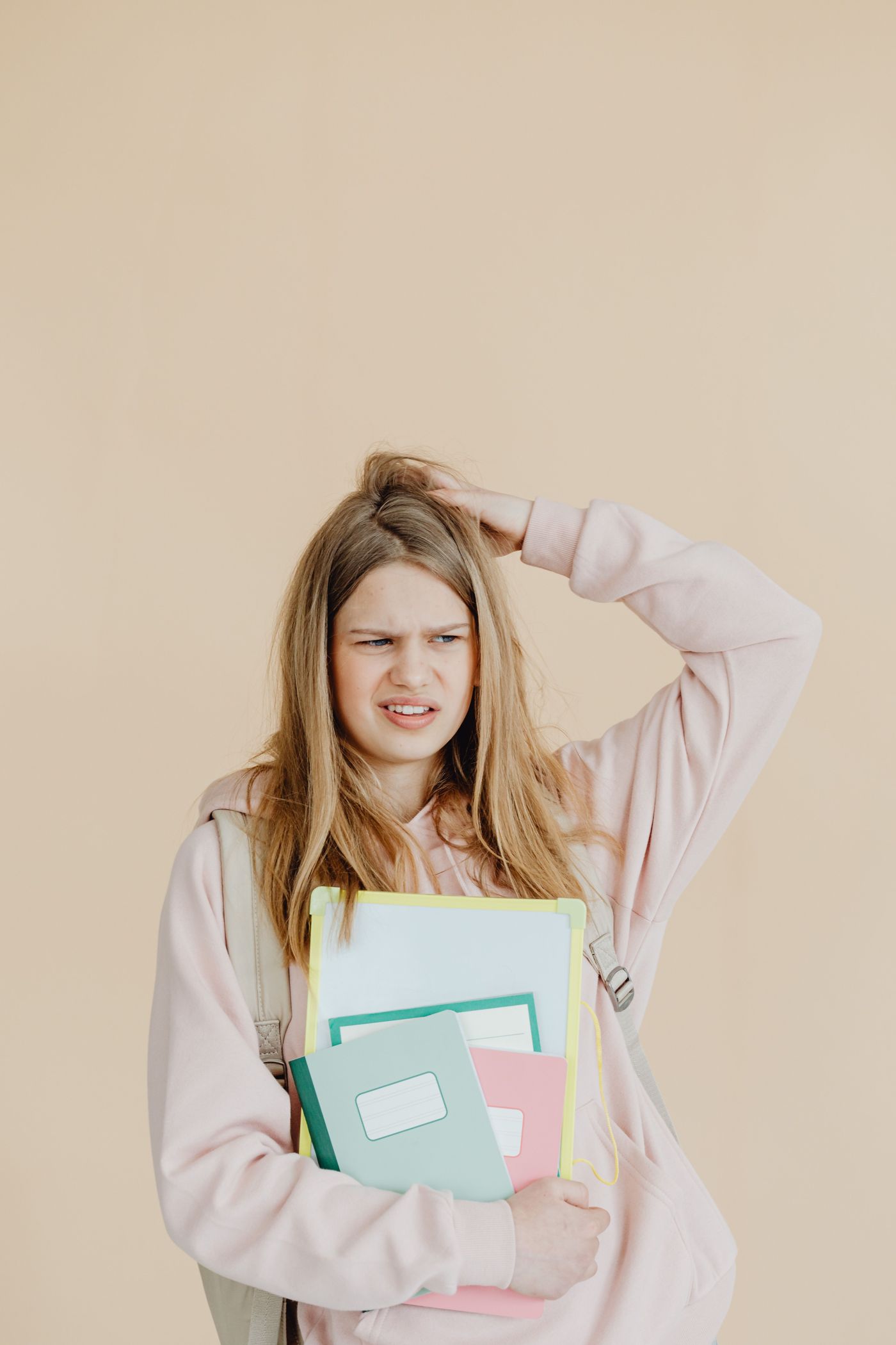 A puzzled student scratching her head while holding a stack of notebooks