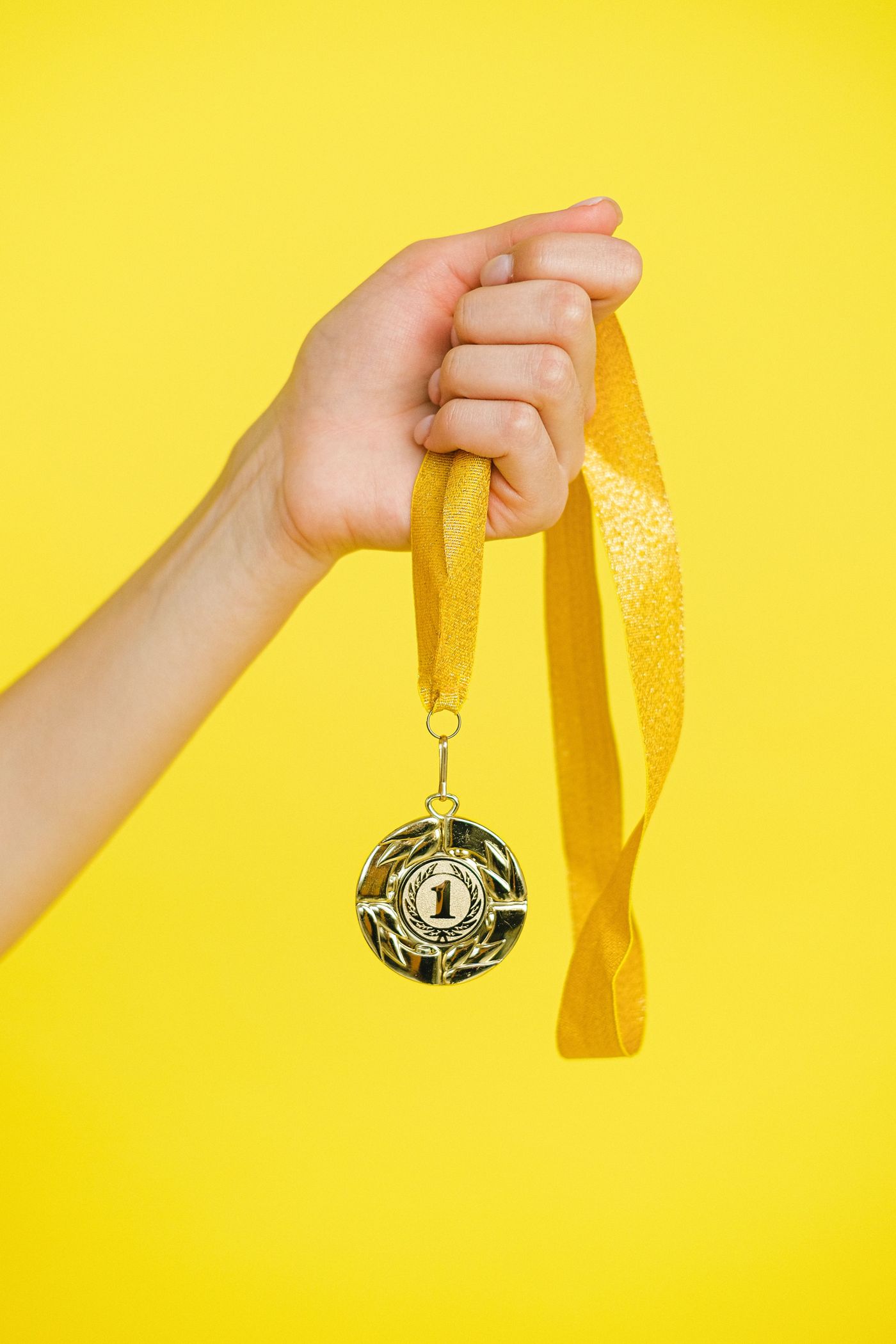 A hand holding up a gold number-one medal on a ribbon against a yellow background