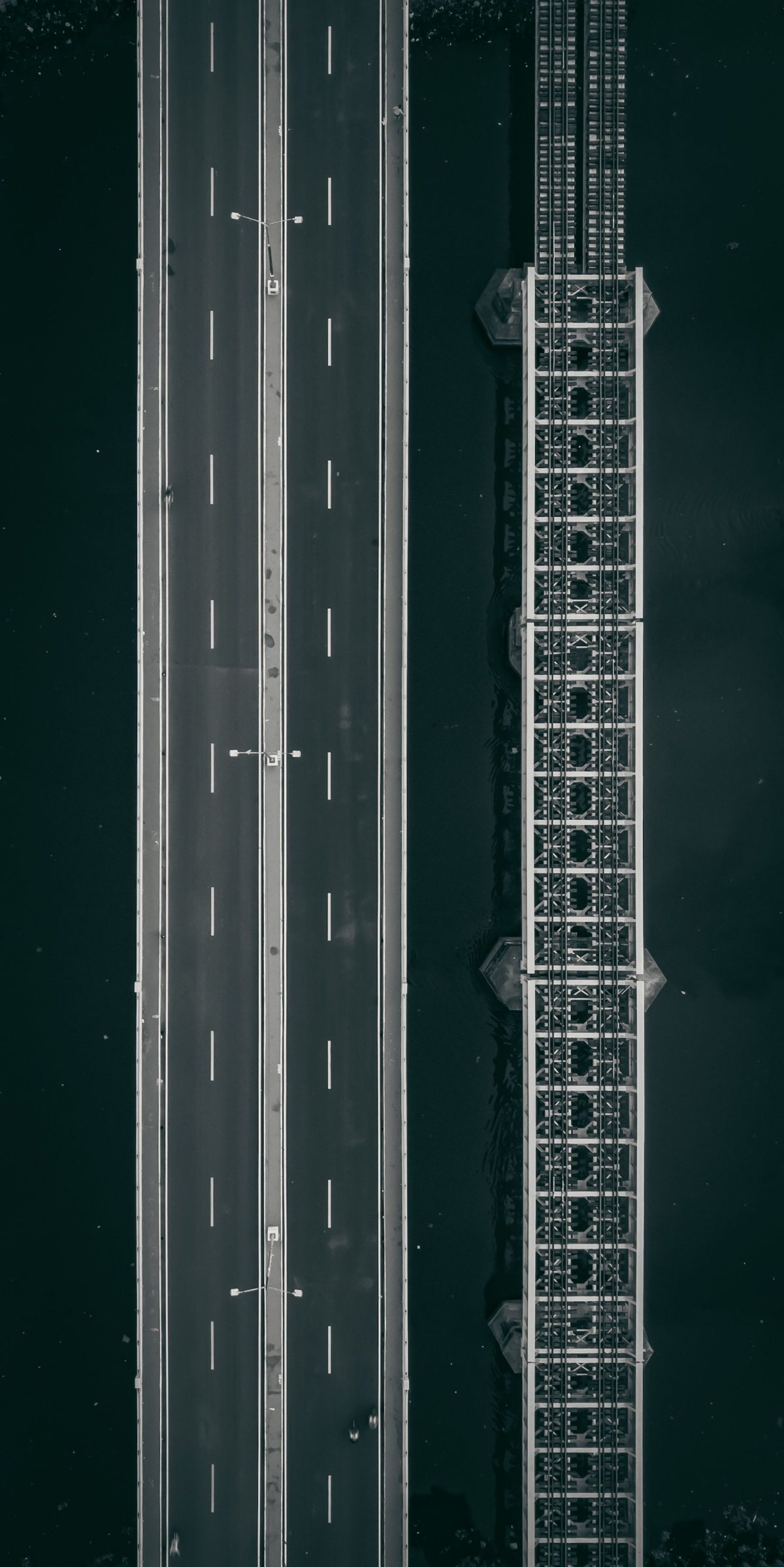 An aerial view of a road bridge and a rail bridge running side by side over dark water
