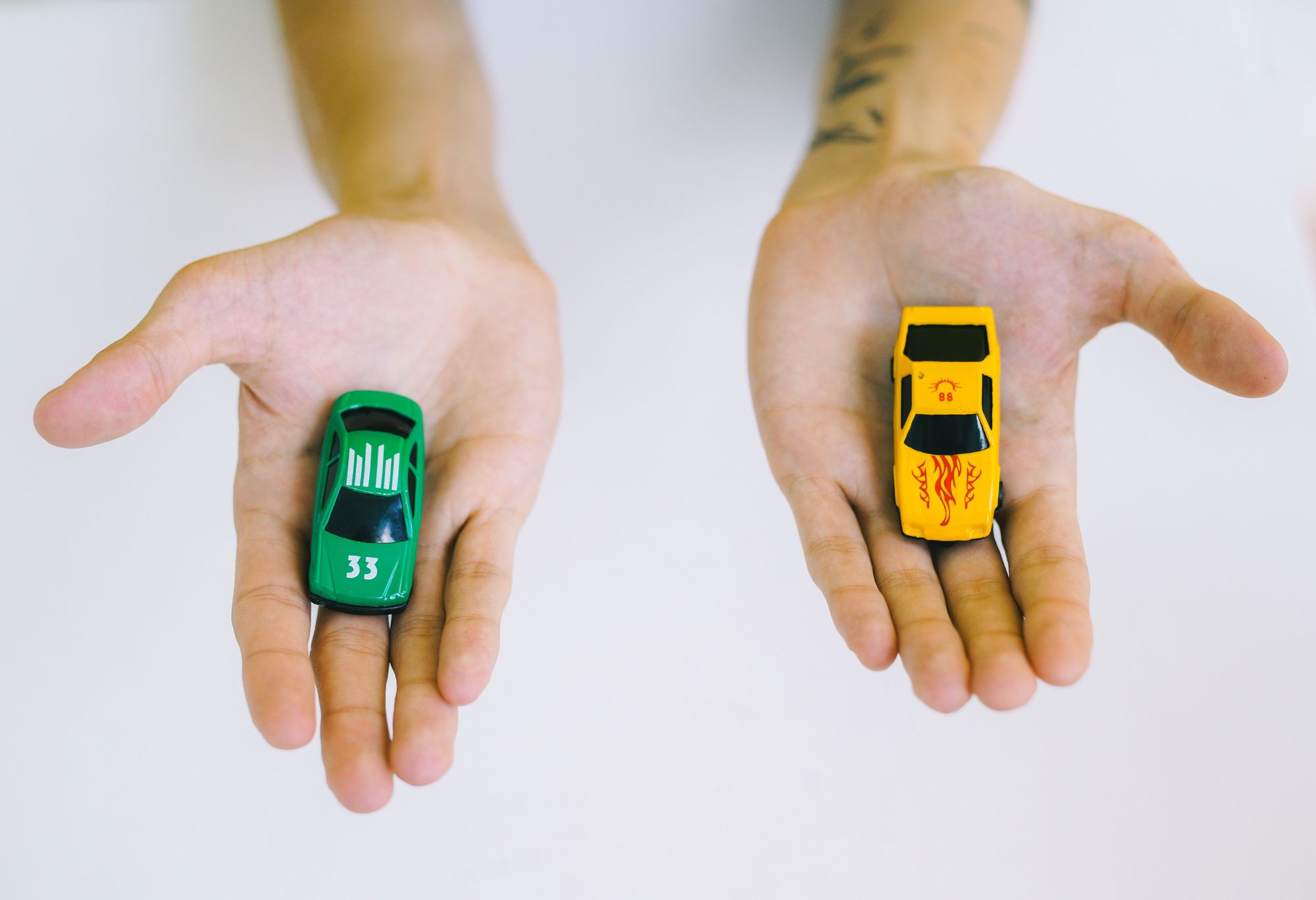 Two open hands, one holding a green toy car and the other a yellow one