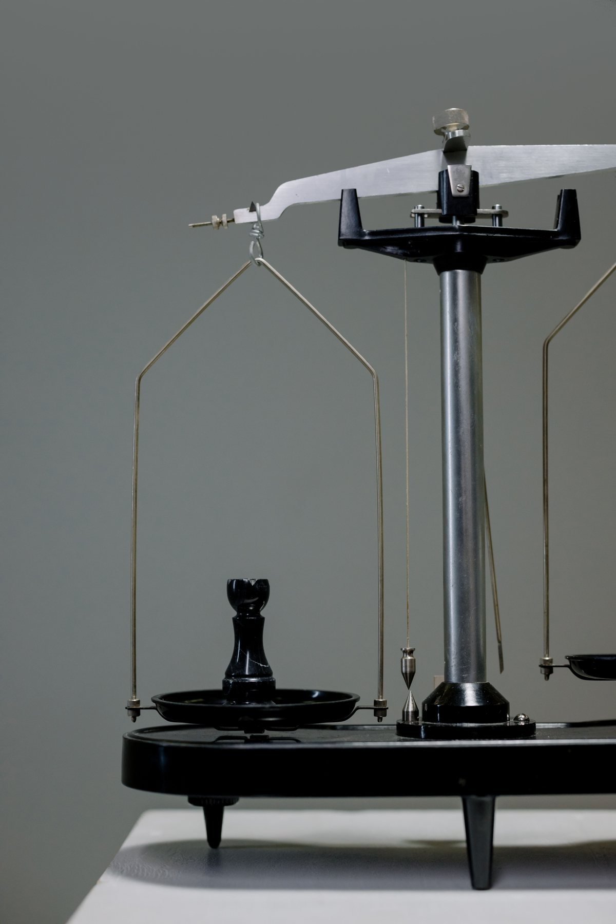 A black chess rook resting on one pan of a vintage balance scale against a grey wall.